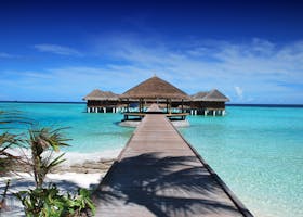 Scenic view of a wooden boardwalk leading to serene overwater bungalows at an island resort.